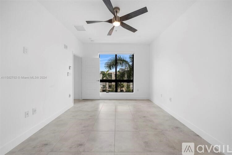 A spacious room with a ceiling fan and a view of a palm tree through the window.