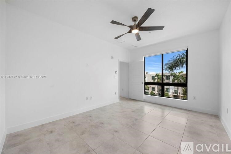 A spacious room with a ceiling fan and a view of a building through the window.