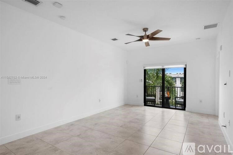 A spacious living room with a ceiling fan and sliding glass doors leading to a balcony.
