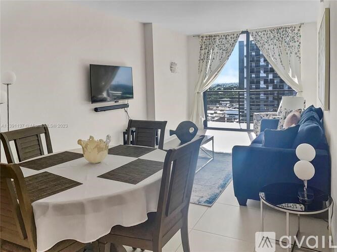 A living room with a television, a dining table with chairs, and a view of a building outside the window.