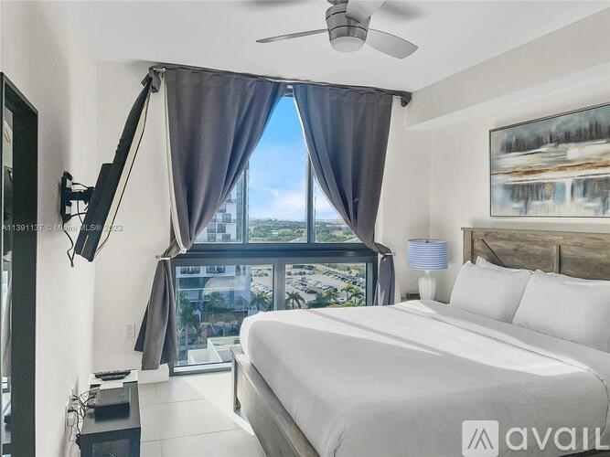A bedroom with a large bed, a ceiling fan, and a view of the city through the window.