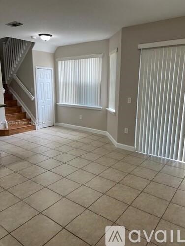 A spacious room with tiled flooring and a staircase on the left side.