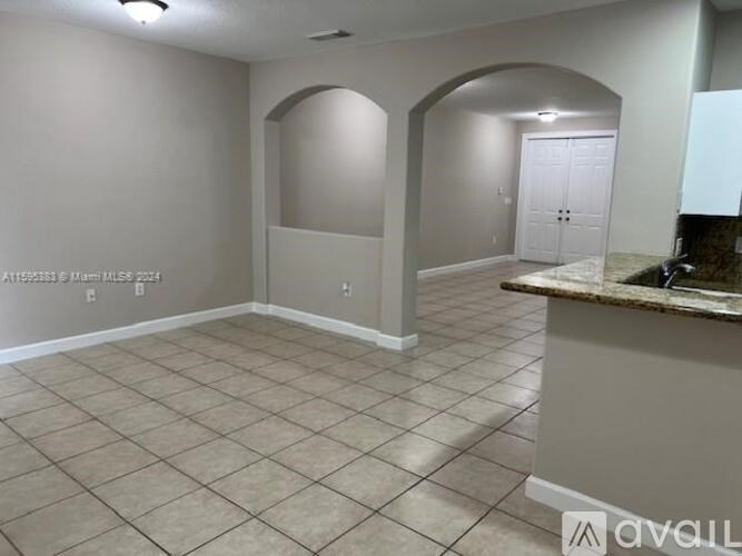 A spacious room with beige tiled flooring and a counter with a backsplash.
