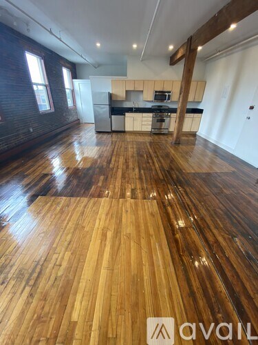 A room with wooden floors and a kitchen area in the background.