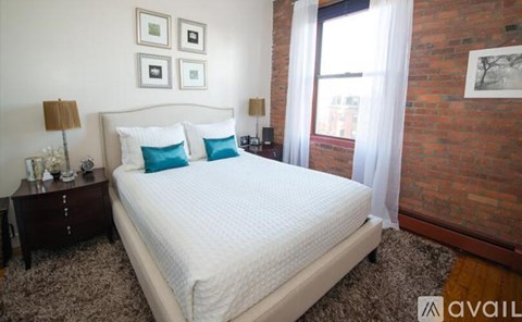 A bedroom with a large bed, a nightstand with a lamp, and a window with curtains.