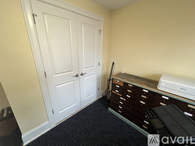 A room with a white door, a printer on a cabinet, and a black floor.
