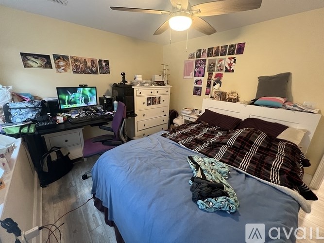 A bedroom with a bed, a desk with a computer, and a ceiling fan.