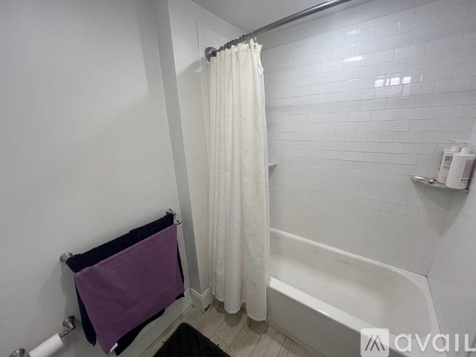 A white tiled bathroom with a purple towel hanging on a rack.
