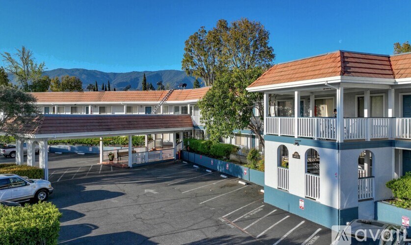 A car is parked in a parking lot in front of a white building with a balcony.