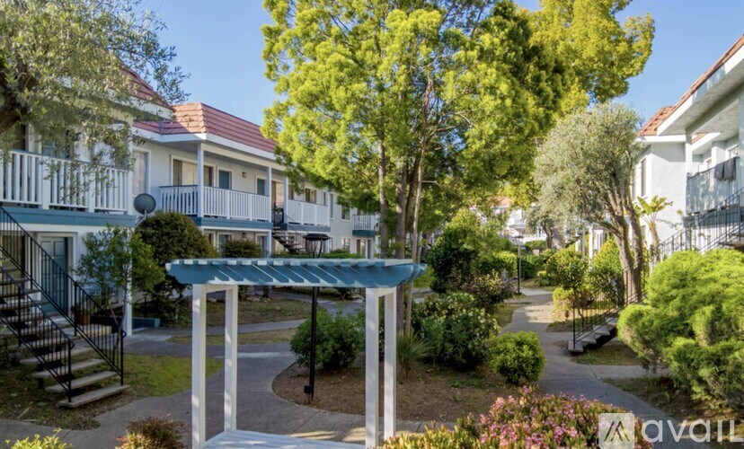 A white building with a red roof is surrounded by green trees and bushes.