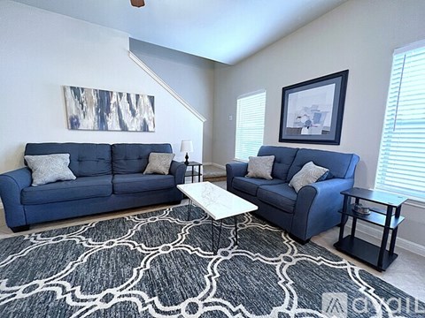 A living room with two blue couches and a patterned rug.