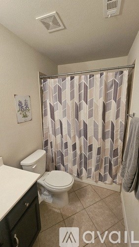 A bathroom with a toilet, a shower curtain, and a plant on the wall.
