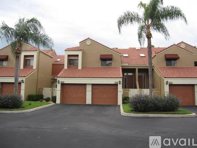 A large house with a driveway and palm trees in front.