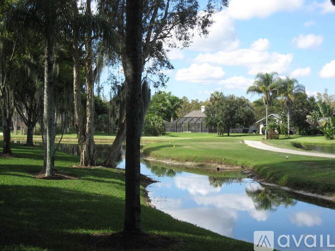 A serene landscape with a pond, trees, and a house in the distance.