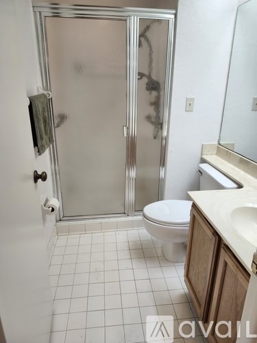 A white tiled bathroom with a toilet, sink, and shower.