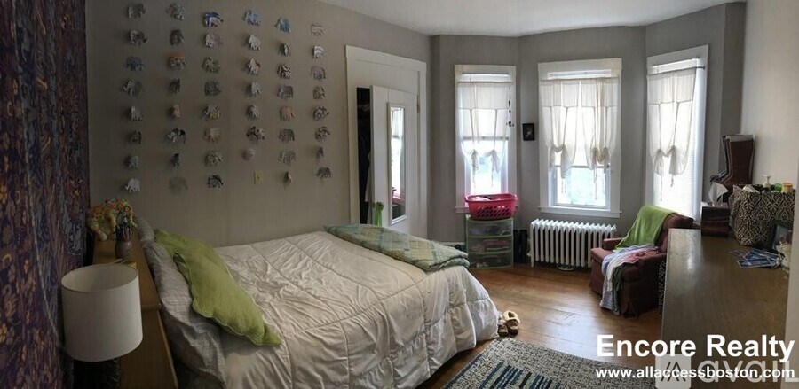 A bedroom with a bed, a chair, and a wall with pictures on it.