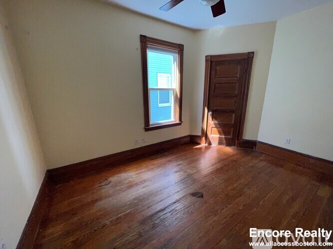 A room with wooden floors and a window with a view of a building outside.