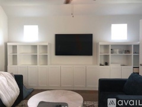 A living room with a black couch, a white coffee table, and a television on a white wall.