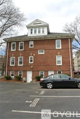 A black car is parked in a parking lot in front of a brick building.