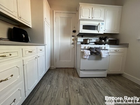 A kitchen with white cabinets and a white stove top oven.