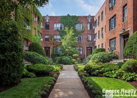A pathway leads through a well-manicured garden in front of a brick building.