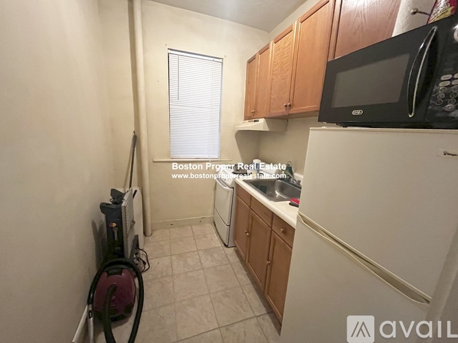 A kitchen with a white refrigerator, a black microwave, and wooden cabinets.
