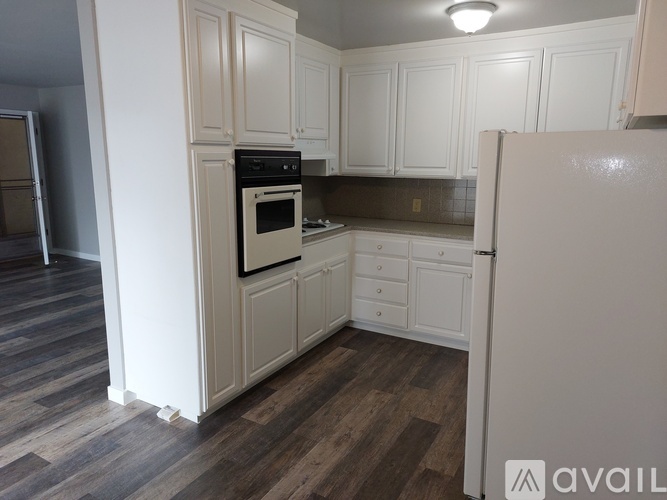 A white refrigerator in a kitchen with wooden floors and white cabinets.