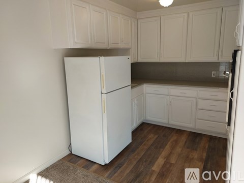 A white refrigerator in a kitchen with wooden floors and white cabinets.