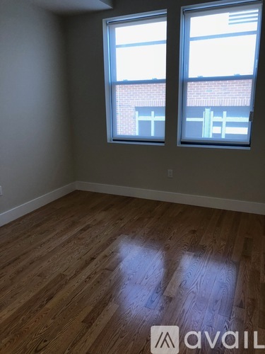 A room with wooden flooring and two windows.
