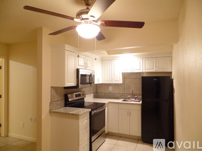 A kitchen with a black refrigerator, white cabinets, and a ceiling fan.