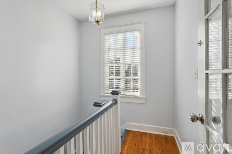 A room with a window covered by white blinds and a chandelier hanging from the ceiling.