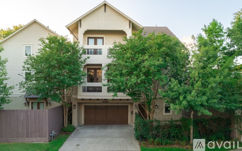 A two-story house with a garage is surrounded by greenery.