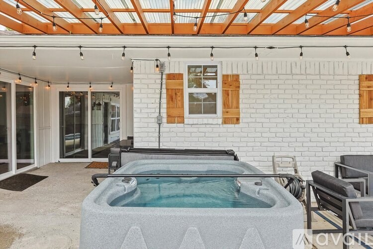 A hot tub is in the middle of a patio with a white brick wall and a glass door.