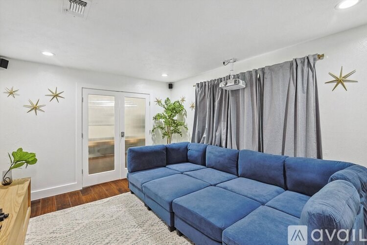 A blue couch is in the middle of a room with a white ceiling and a plant to the left.