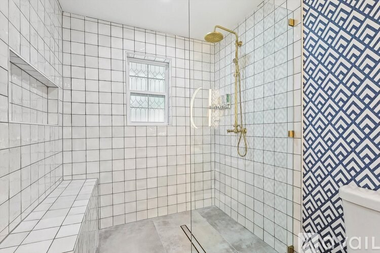 A white tiled bathroom with a shower and a window.