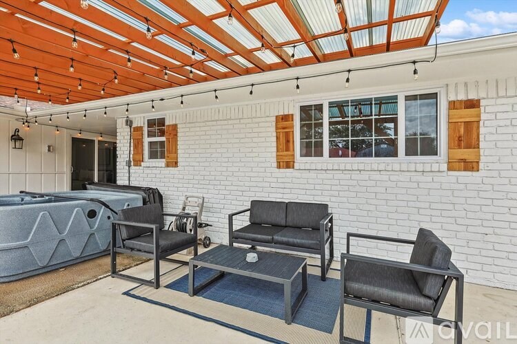 A patio with a hot tub, couch, and chairs under a wooden pergola.