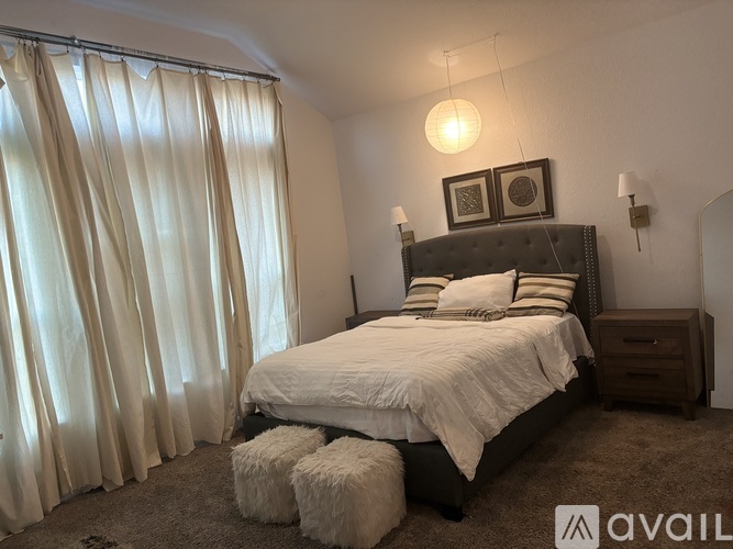 A bedroom with a large bed, a nightstand, and a window with curtains.