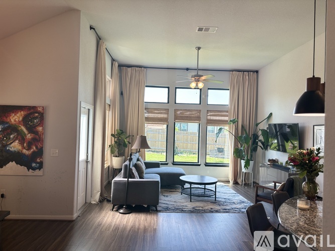 A living room with a grey sofa, a grey armchair, a grey coffee table, a grey rug, a black floor lamp, a black ceiling fan, a black hanging light fixture, a black pendant light, a black