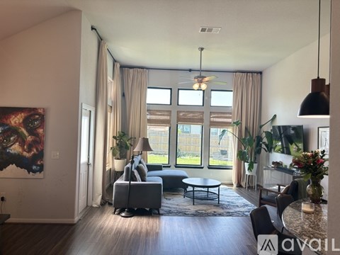 A living room with a grey sofa, a grey armchair, a grey coffee table, a grey rug, a black floor lamp, a black ceiling fan, a black hanging light fixture, a black pendant light, a black
