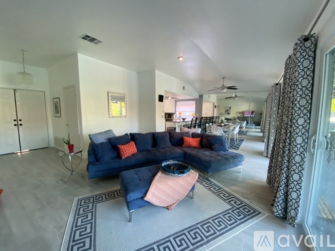 A living room with a blue couch and a pink ottoman.