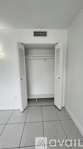 A white closet with a door open and a small vent on the ceiling.