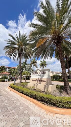 A sign for Gran Vista Gated Communities stands in front of a row of palm trees.