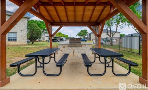 A picnic area with two tables and benches under a wooden canopy.