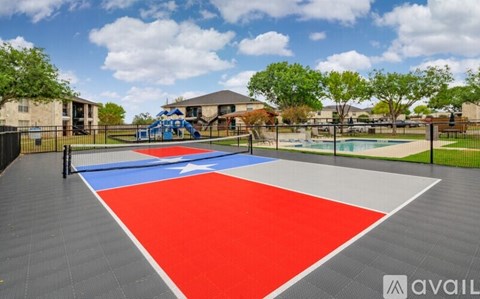 A basketball court with a red and blue surface is surrounded by a black fence.