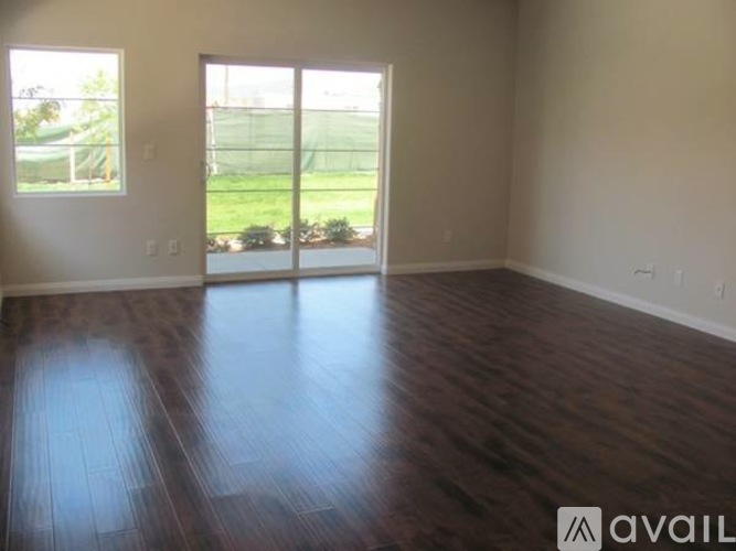 A room with wooden floors and a view of a green lawn through the sliding glass doors.