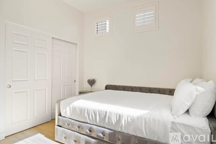 A white bedroom with a bed, pillows, and a heart-shaped object on the bed.