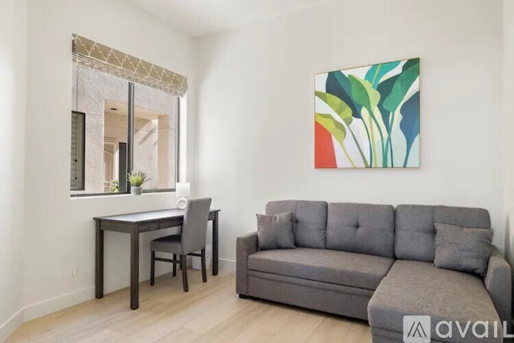 A living room with a grey couch, a desk with a chair, and a painting on the wall.