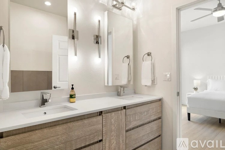 A bathroom with a sink, mirror, and a bed in the background.