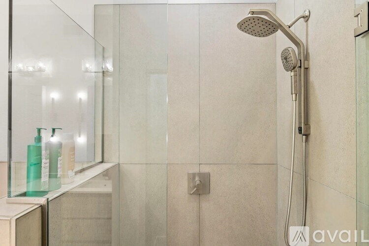 A shower area with a glass door and a glass shelf with three bottles on it.