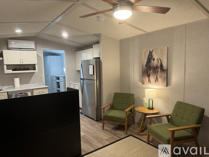 A room with a refrigerator, a chair, and a painting of a horse.